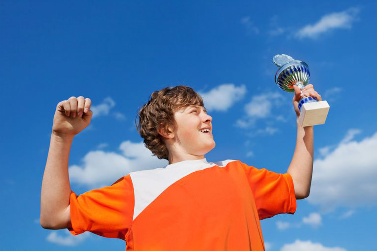 Kid in orange sports jersey holding trophy and flexing his muscles