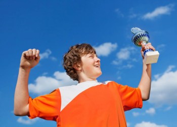 Kid in orange sports jersey holding trophy and flexing his muscles