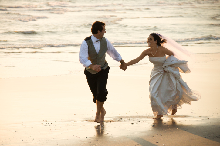 Caucasian prime adult male groom and female bride running barefoot on beach.