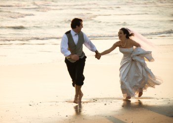 Caucasian prime adult male groom and female bride running barefoot on beach.