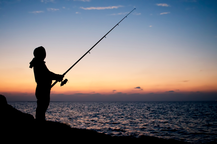 Man fishing silhouette at sunset on a seashore
