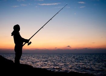 Man fishing silhouette at sunset on a seashore