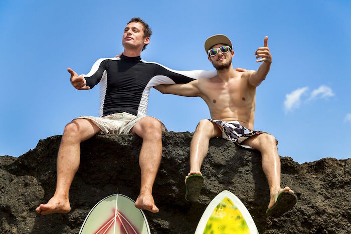 two friend surfer sitting on a rock showing sign ok