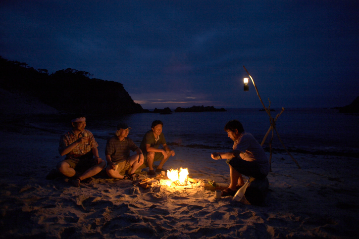 Friends sitting around campfire on beach at night