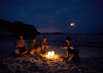 Friends sitting around campfire on beach at night