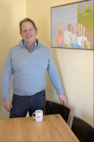 Colin Ambrose, proprietor of Estia's Little Kitchen, host to 20 years of showing local art, standing near his family portrait by Valerie Suter who is the current exhibitor.