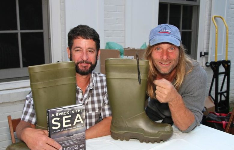 Montauk-based authors John Aldridge and Anthony Sosinski pose with their latest novel and the pair of boots John used to keep him afloat and alive during his harrowing ordeal