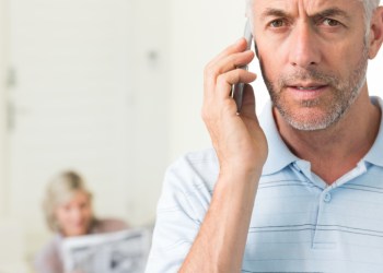 Mature man using cellphone with woman reading newspaper in background