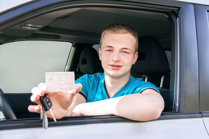 Car driver. Caucasian teen boy showing driver license, car key.