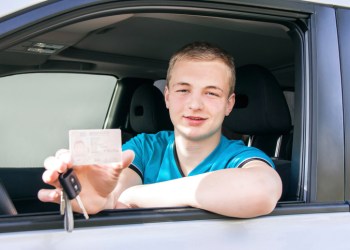 Car driver. Caucasian teen boy showing driver license, car key.