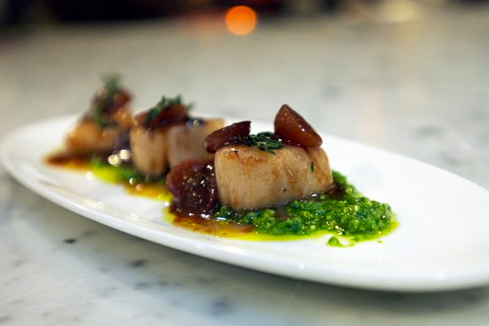 Three scallops on a plate with sauce and garnish