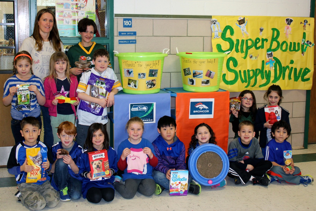 Lauren Squires and Teaching Assistant Charlene Goodman with the 2nd grade students holding some of the many donations and wearing some of their favorite team's jerseys.
