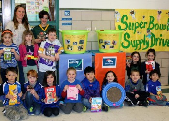 Lauren Squires and Teaching Assistant Charlene Goodman with the 2nd grade students holding some of the many donations and wearing some of their favorite team's jerseys.
