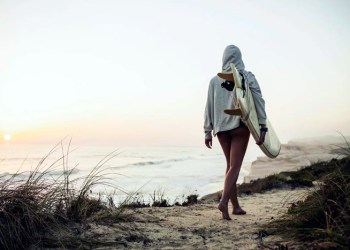 Surfer girl in hoodie checks the waves