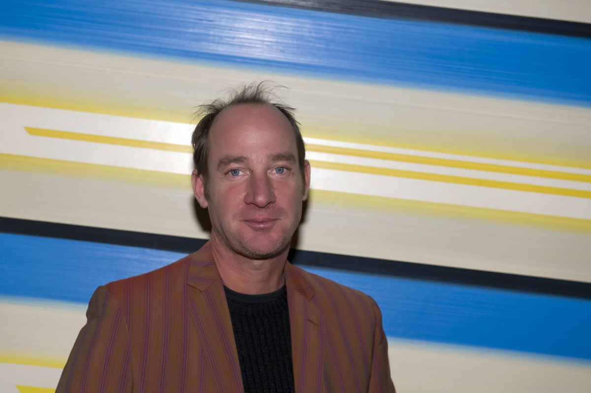 PAINTER JAMESON ELLIS STANDING IN FRONT OF ONE OF HIS PAINTINGS.