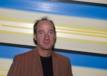 PAINTER JAMESON ELLIS STANDING IN FRONT OF ONE OF HIS PAINTINGS.