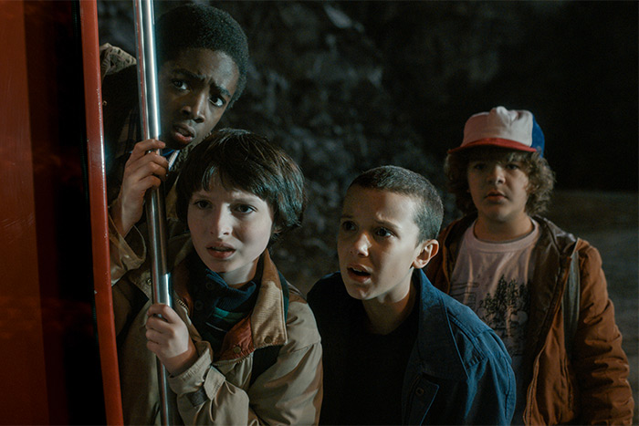 The cast of Stranger Things, four kids looking scared in the dark outside