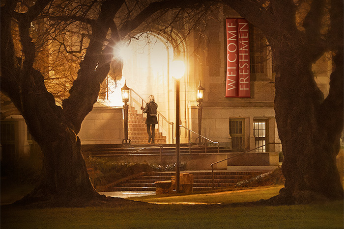 A female college student walking into a building late at night, with a welcome freshman banner hanging above - from the poster for the film "The Hunting Ground"
