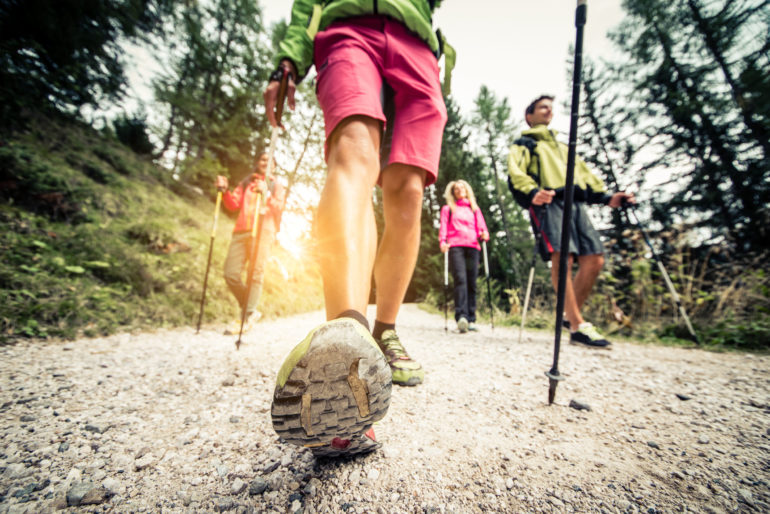 roup of hikers with backpacks and sticks walking on a mountain at sunset - four friends making an excursion in the nature