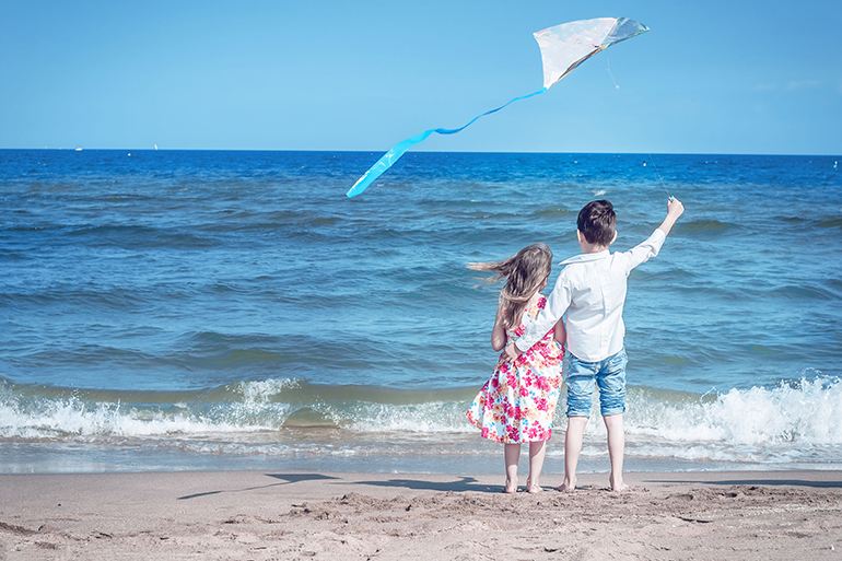 boy and girl at the beach with a kite. freedom, carefree childhood and hope. brother and sister together.