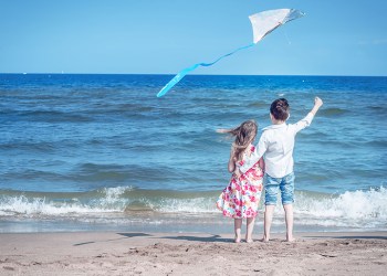boy and girl at the beach with a kite. freedom, carefree childhood and hope. brother and sister together.