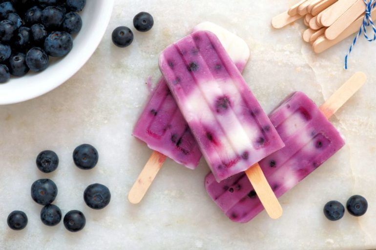 40300500 - blueberry vanilla popsicles in a cluster with fresh berries on a white marble background
