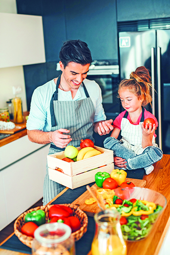 Happy father and daughter picking fruits and vegetables in the kitchen.