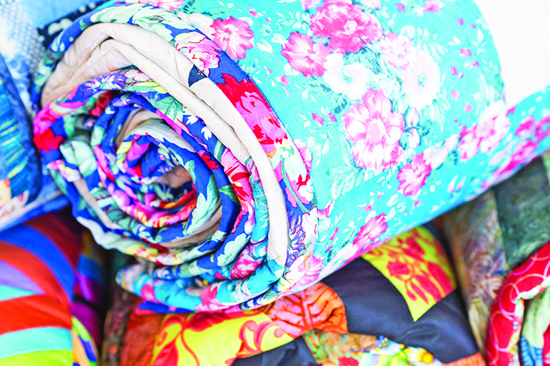 83043225 - homemade, garment industry, craft concept. macro on a perfectly sewn part of the bedspread for the bed with images of weightless pink carnations twisted into roll