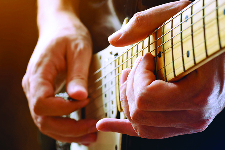 27119465 - man playing guitar on a stage. musical concert. close-up view.