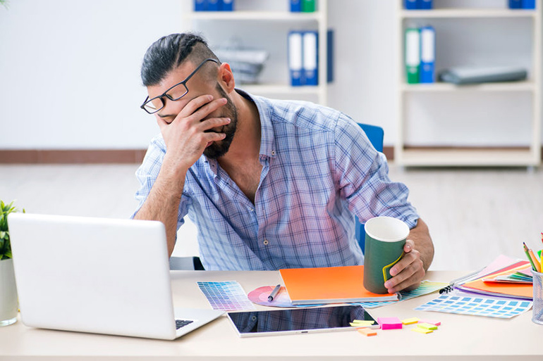 Upset interior designer sitting at his desk with a hand over his face