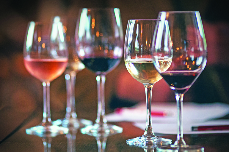 Closeup of five wineglasses arranged one next to the other, half full with several sorts of wines, red, white and rose wines. Glasses are on the table, there are some papers and pens in background as this was the detail from winetasting. Lit from both sides.