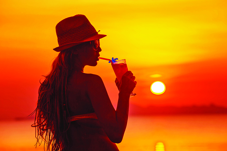 57528606 - closeup portrait of woman in hat with cocktail at tropical red sunset background.