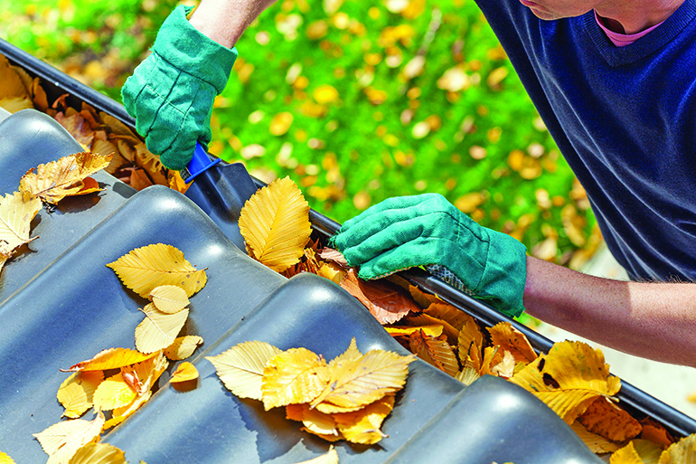 Man cleaning the gutter from autumn leaves