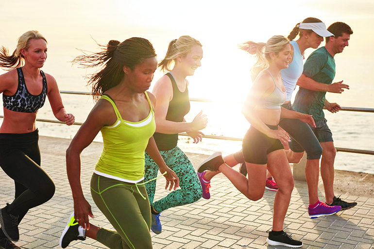 54740064 - portrait of healthy young men and women running race on seaside promenade. group of young people sprinting outdoors at sunset.