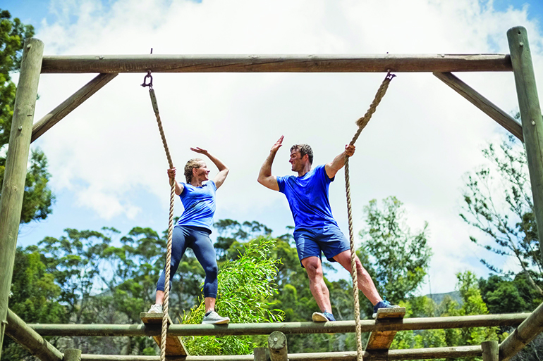 Fit man and woman giving high five during obstacle course in boot camp