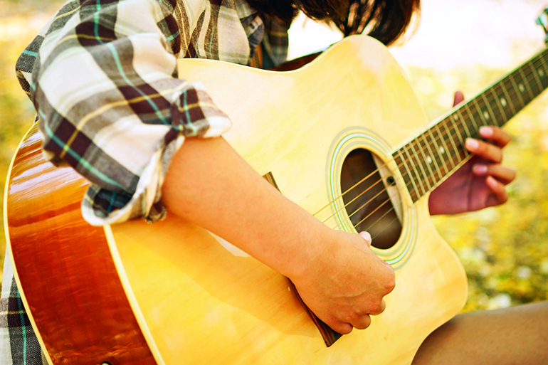 Closeup of young woman's hands playing acoustic guitar outdoors