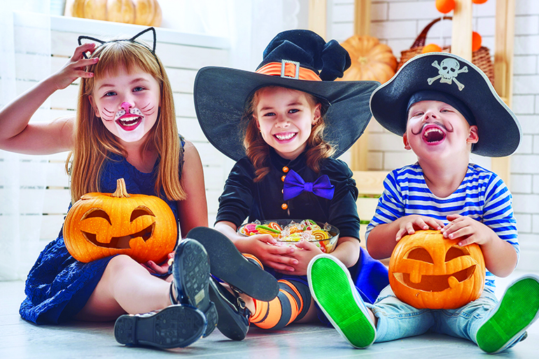 62765546 - happy brother and two sisters on halloween. funny kids in carnival costumes indoors. cheerful children play with pumpkins and candy.