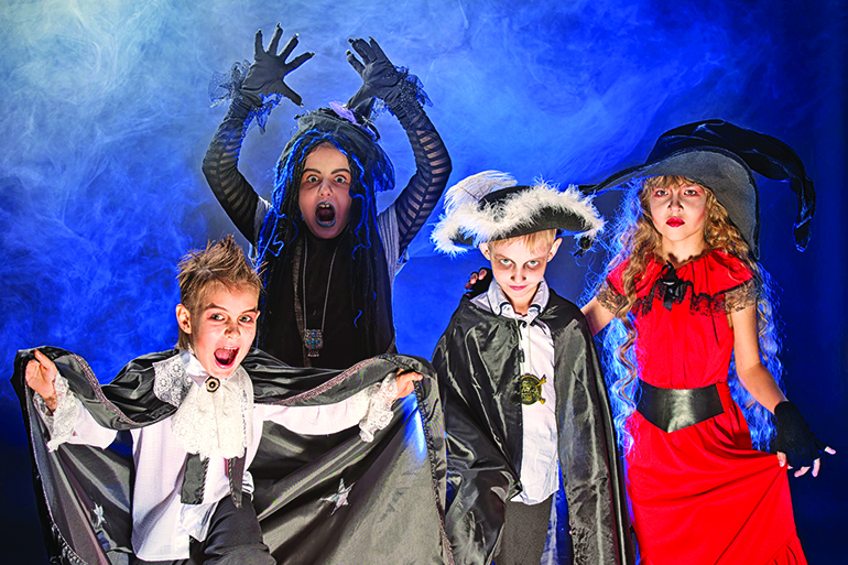 Cheerful children in halloween costumes posing over dark background.
