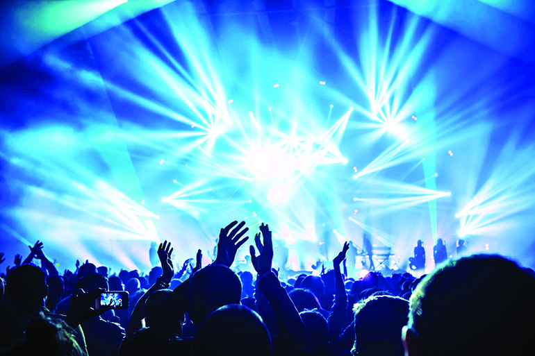 Large group of happy people enjoying rock concert, clapping with raised up hands, blue lights from the stage, new year celebration concept