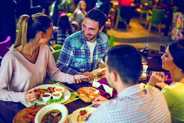 Young woman using mobile phone during lunch with friends in a restaurant.