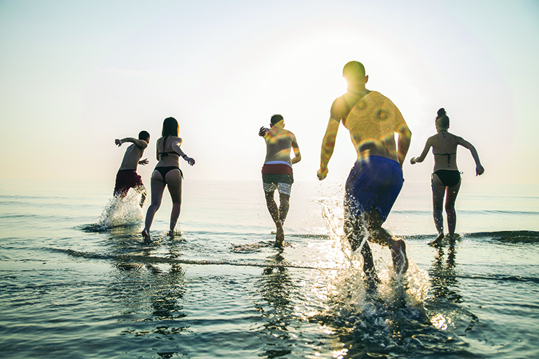 Group of happy friends running in to water at sunset - Silhouettes of active people having fun on the beach on vacation - Tourists going to swim on a tropical island