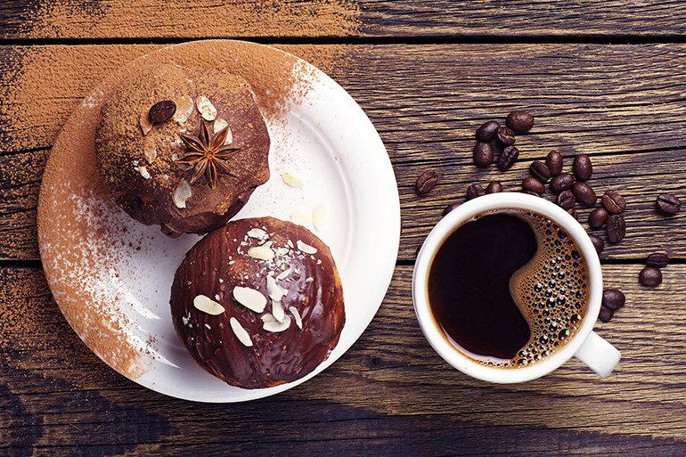 top view of a cup of coffee and cupcake with chocolate and nuts on wooden table