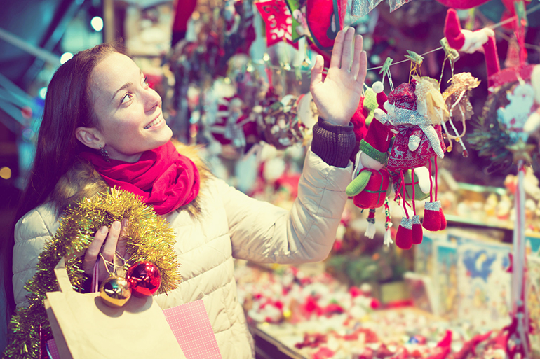 Cheerful girl customer near counter with Christmas gifts in evening time selects gifts for loved ones