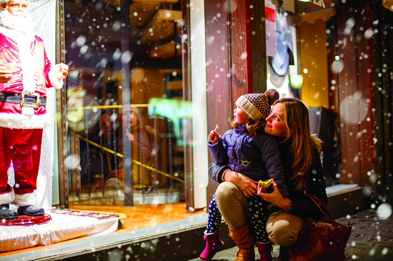 little toddler girl with mother on christmas market. funny happy kid making window shopping with santa claus. holidays, christmas, childhood and people concept. family during winter snowfall