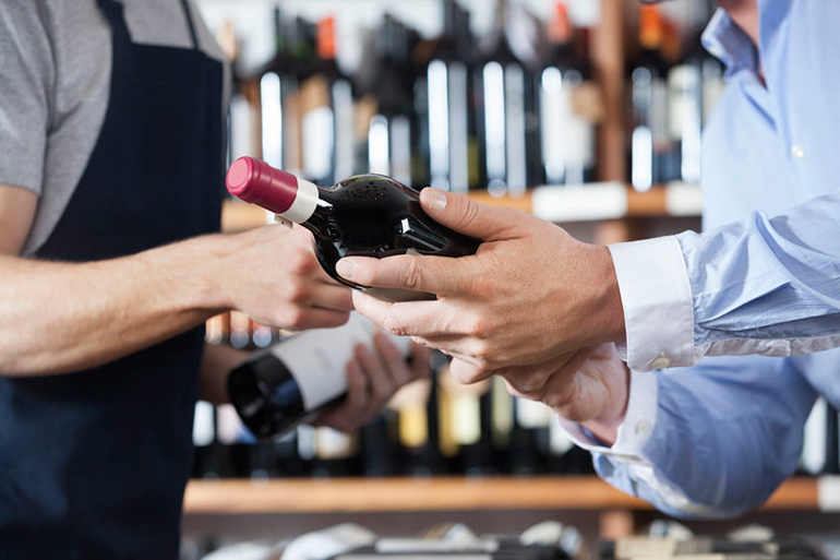 Liquor store worker and customer discussing a bottle of red wine