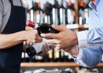 Liquor store worker and customer discussing a bottle of red wine