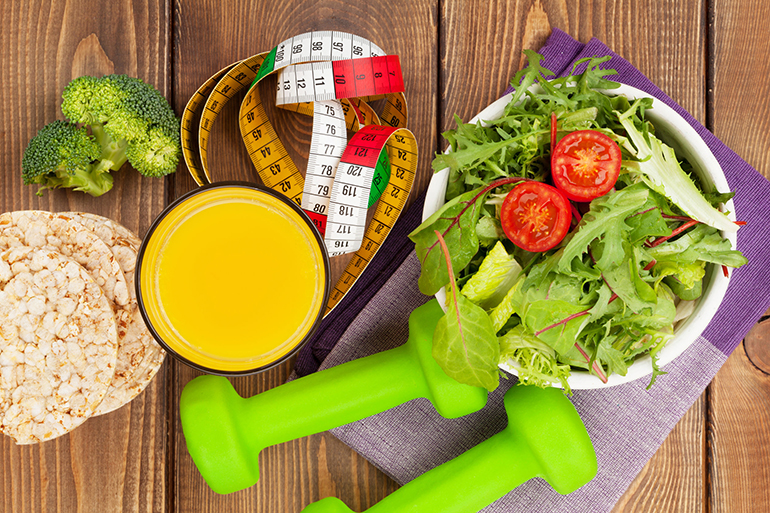 Dumbells, tape measure and healthy food over wooden table. Fitness and health