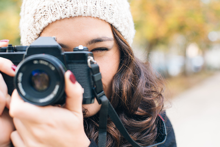 Close up of a young beautiful woman with an analog camera shooting to you in autumn