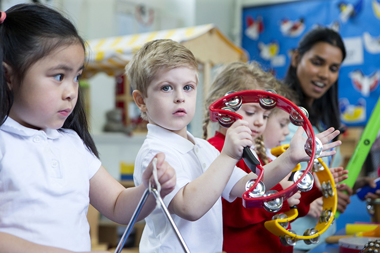 Nursery children playing with musical instruments in the classroom. One little boy is looking at the camera with a tambourine.