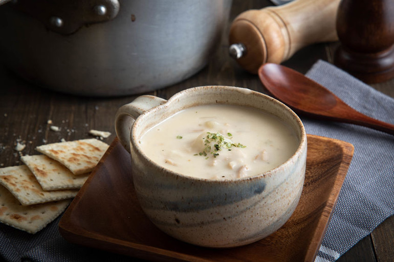 New England clam chowder in cermamic bowl with pepper grinder, pot and wooden spoon